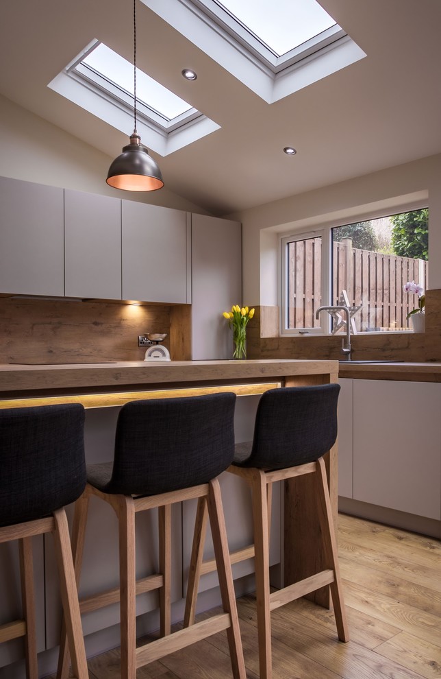 Inspiration for a medium sized modern kitchen in Other with a single-bowl sink, flat-panel cabinets, white cabinets, wood worktops, wood splashback, stainless steel appliances, light hardwood flooring and an island.