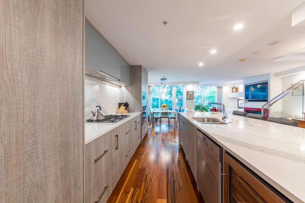 This is an example of a medium sized contemporary single-wall open plan kitchen in Vancouver with a double-bowl sink, flat-panel cabinets, grey cabinets, quartz worktops, porcelain splashback, stainless steel appliances, medium hardwood flooring and an island.