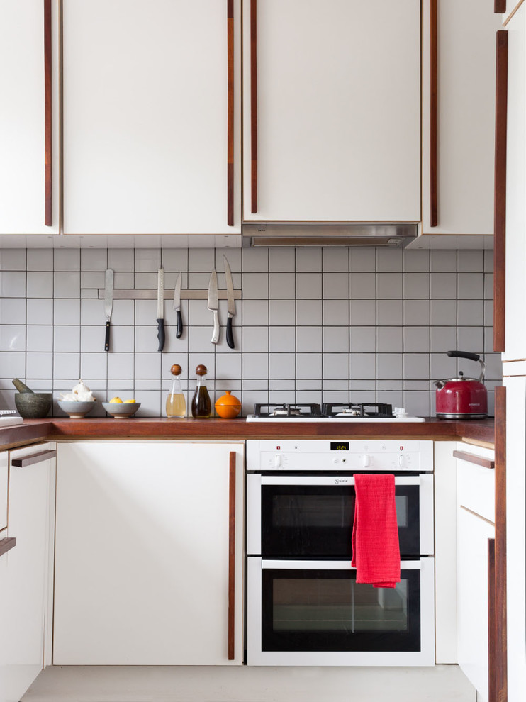Foto på ett 50 tals u-kök, med släta luckor, vita skåp, träbänkskiva, vitt stänkskydd och vita vitvaror