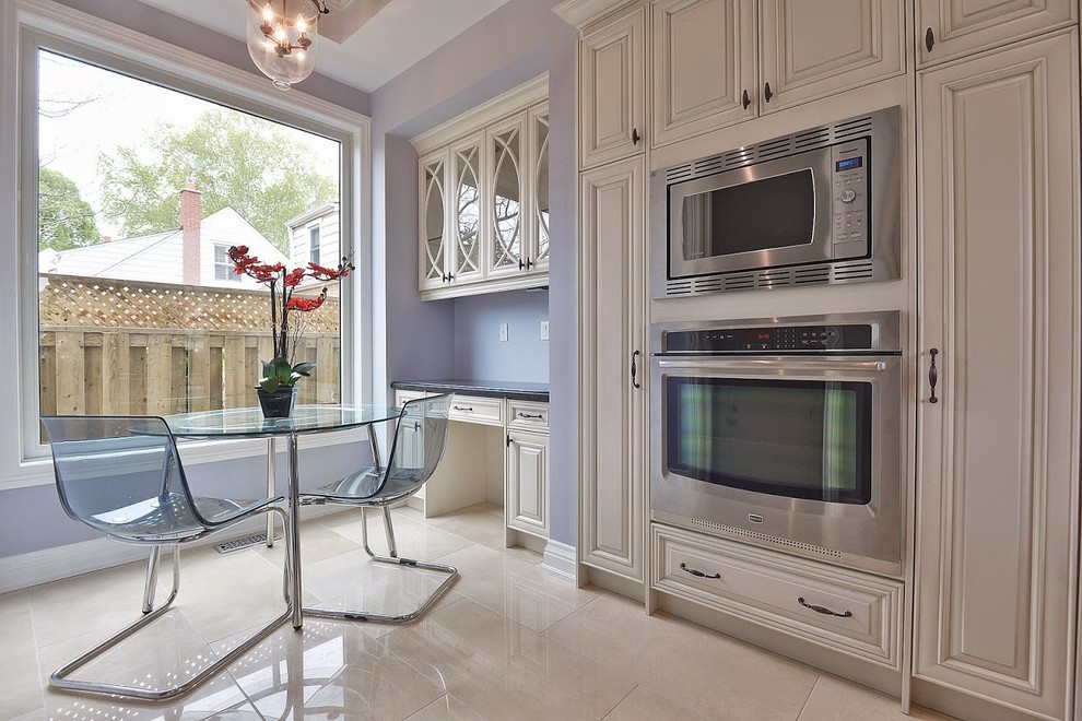 Example of a large classic l-shaped limestone floor eat-in kitchen design in Toronto with beige cabinets, granite countertops, multicolored backsplash, glass sheet backsplash, stainless steel appliances and an island