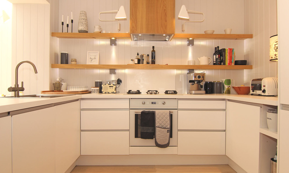 Foto på ett litet maritimt kök, med en integrerad diskho, släta luckor, vita skåp, vitt stänkskydd, glaspanel som stänkskydd, färgglada vitvaror, ljust trägolv, bänkskiva i kvarts och en halv köksö