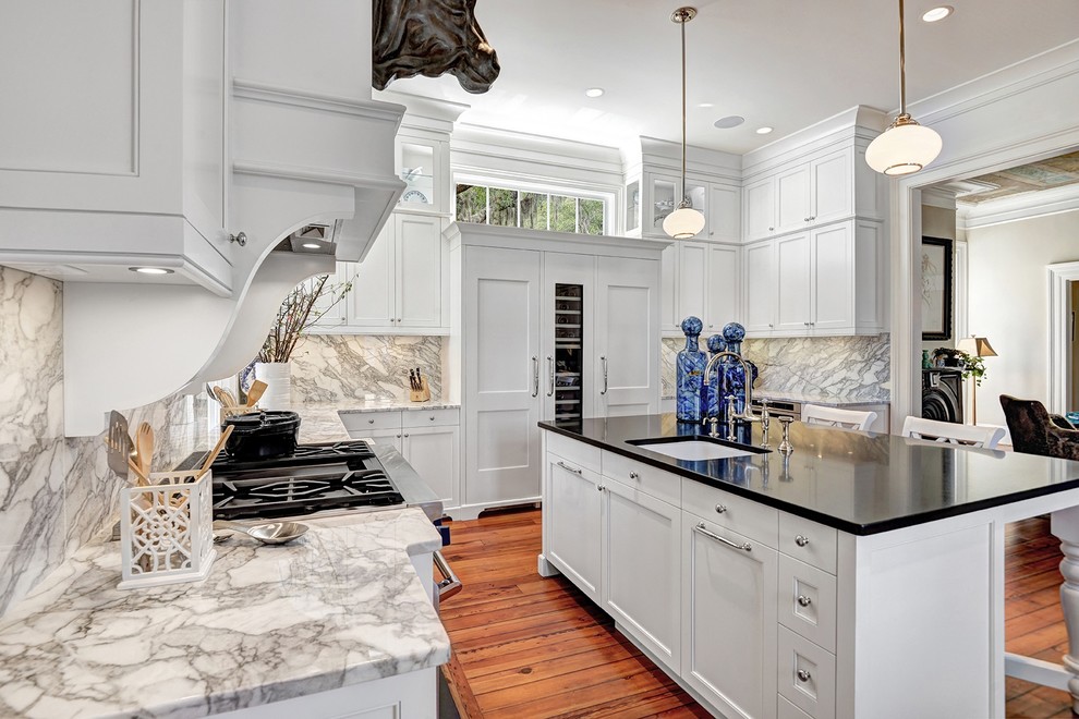Example of a large transitional u-shaped medium tone wood floor kitchen design in Charleston with an undermount sink, beaded inset cabinets, white cabinets, marble countertops, gray backsplash, stone slab backsplash, paneled appliances and an island