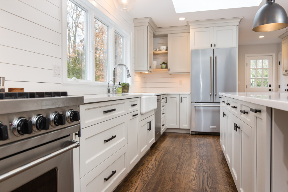 Foto på ett stort lantligt vit kök, med en rustik diskho, skåp i shakerstil, grå skåp, bänkskiva i kvarts, vitt stänkskydd, stänkskydd i trä, rostfria vitvaror, mellanmörkt trägolv, en köksö och brunt golv