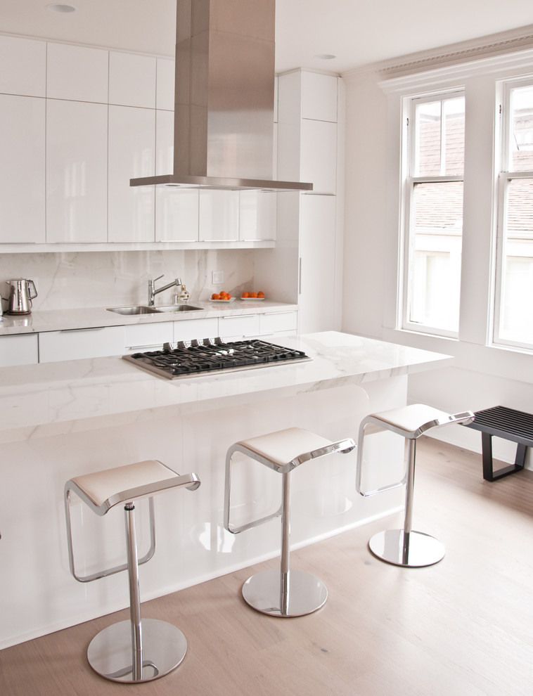 Open concept kitchen - mid-sized modern galley light wood floor open concept kitchen idea in San Francisco with an undermount sink, flat-panel cabinets, white cabinets, marble countertops, white backsplash, stone slab backsplash, white appliances and a peninsula