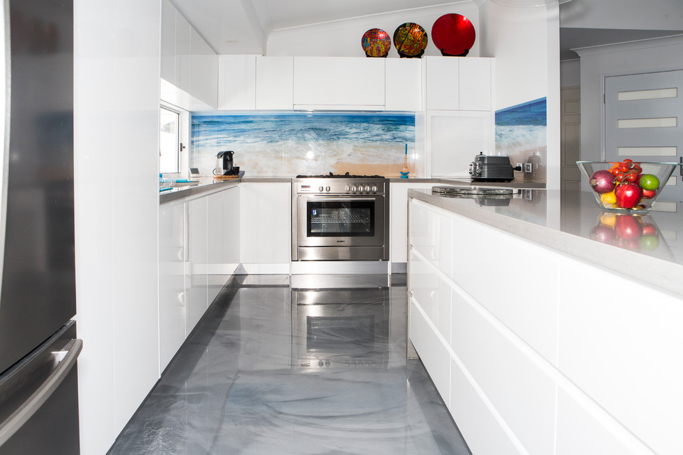 Bild på ett funkis kök, med en undermonterad diskho, släta luckor, vita skåp, bänkskiva i kvarts, flerfärgad stänkskydd, glaspanel som stänkskydd, rostfria vitvaror, betonggolv och en köksö