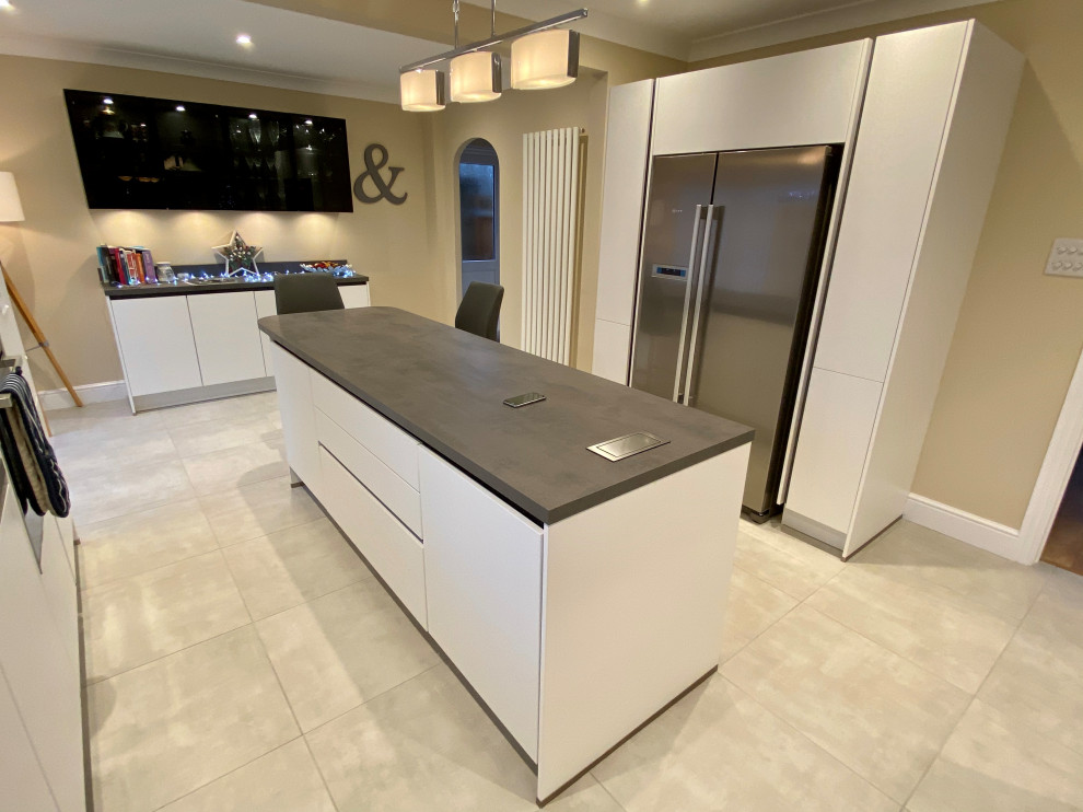 This is an example of a large contemporary l-shaped open plan kitchen in Sussex with a built-in sink, flat-panel cabinets, white cabinets, laminate countertops, grey splashback, black appliances, vinyl flooring, multiple islands, beige floors and grey worktops.