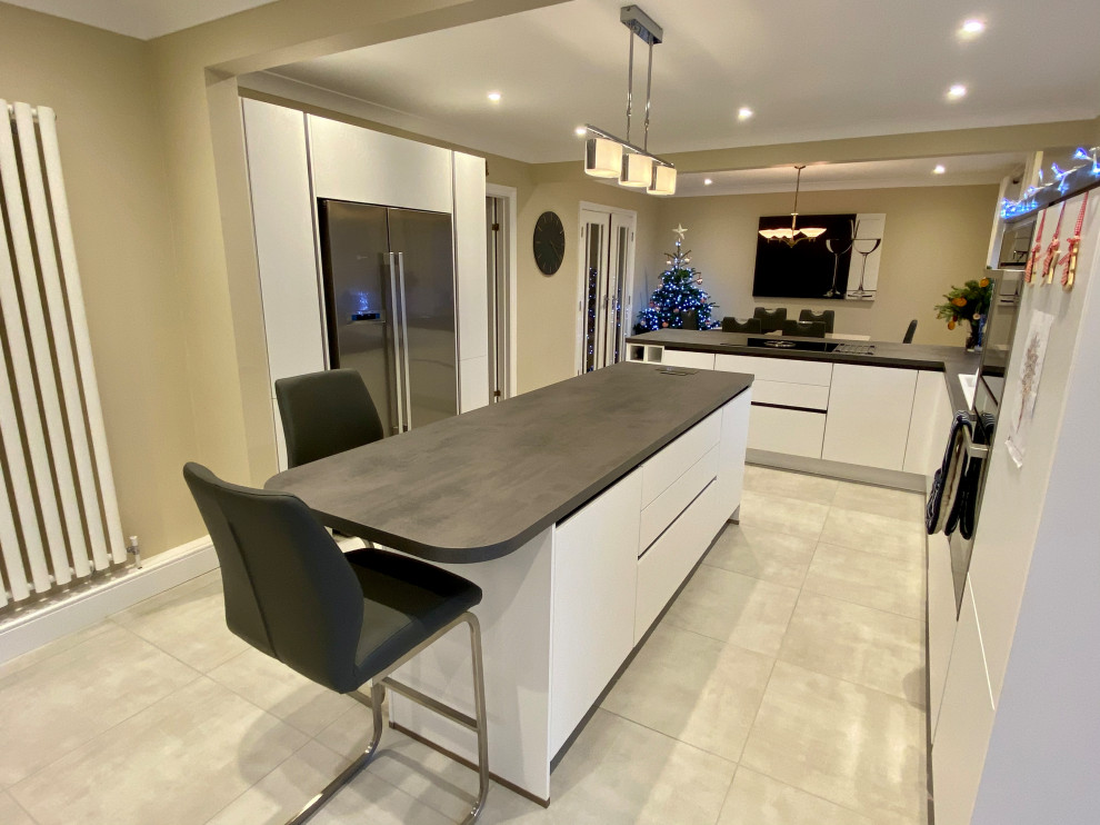 Example of a large trendy l-shaped vinyl floor and beige floor open concept kitchen design in Sussex with a drop-in sink, flat-panel cabinets, white cabinets, laminate countertops, gray backsplash, black appliances, two islands and gray countertops