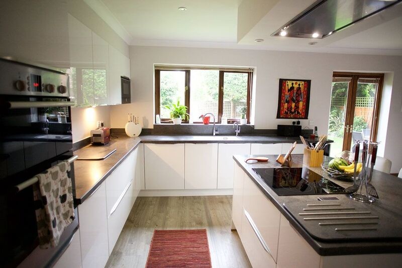 Mittelgroße Moderne Wohnküche in U-Form mit flächenbündigen Schrankfronten, weißen Schränken, Küchengeräten aus Edelstahl und Kücheninsel in Sussex