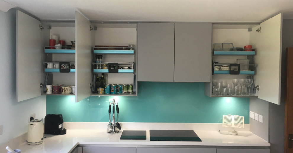 Design ideas for a medium sized contemporary l-shaped open plan kitchen in Sussex with a submerged sink, flat-panel cabinets, grey cabinets, quartz worktops, blue splashback, glass sheet splashback, vinyl flooring, brown floors, white worktops, integrated appliances and an island.