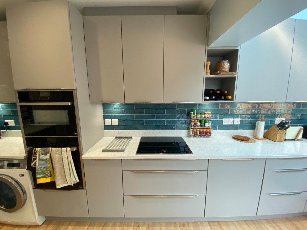 Foto på ett stort funkis vit kök, med en undermonterad diskho, släta luckor, grå skåp, bänkskiva i kvartsit, blått stänkskydd, stänkskydd i keramik, svarta vitvaror, vinylgolv, en köksö och brunt golv