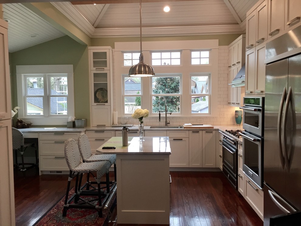 Foto på ett vintage kök och matrum, med en undermonterad diskho, skåp i shakerstil, vita skåp, marmorbänkskiva, vitt stänkskydd, stänkskydd i tunnelbanekakel, rostfria vitvaror, mellanmörkt trägolv och en köksö