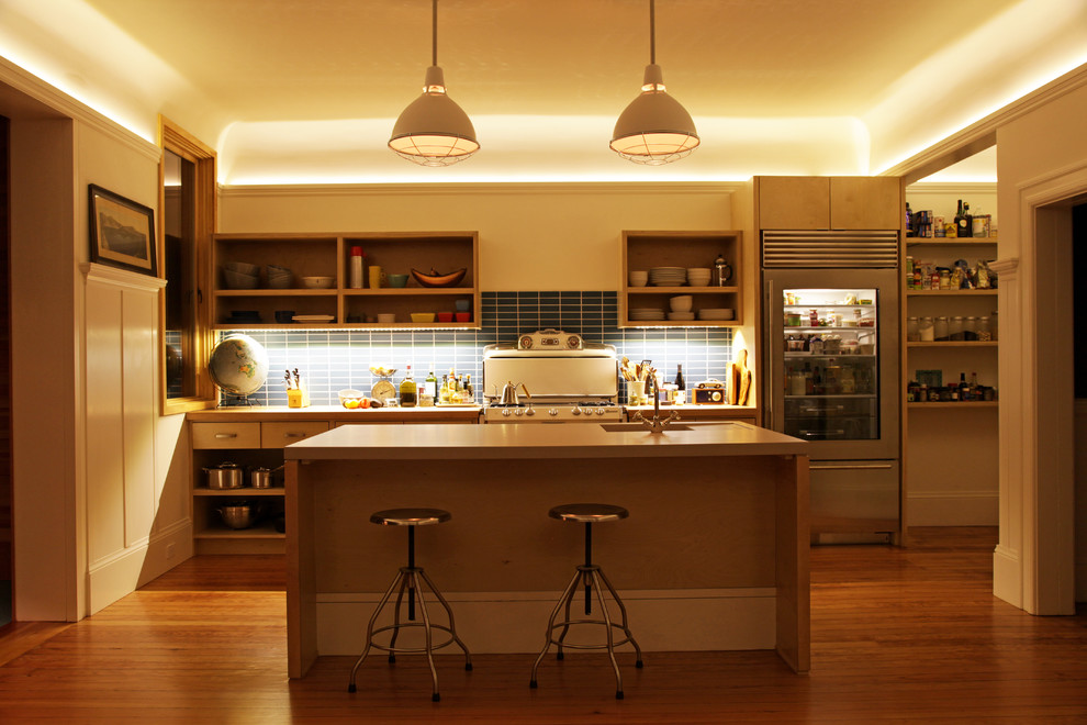Cette image montre une cuisine parallèle design en bois clair avec un placard sans porte, un plan de travail en béton, une crédence bleue, une crédence en céramique, un électroménager en acier inoxydable et un évier intégré.