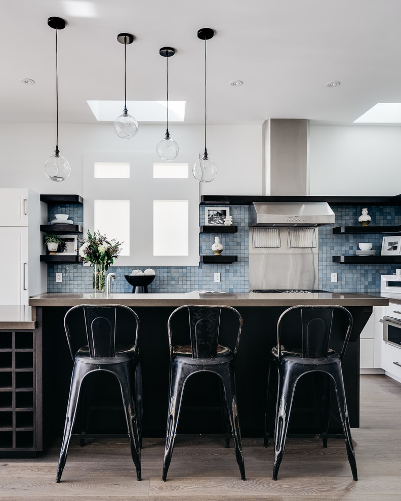 Foto på ett funkis l-kök, med släta luckor, vita skåp, blått stänkskydd, stänkskydd i mosaik, rostfria vitvaror, ljust trägolv och en köksö