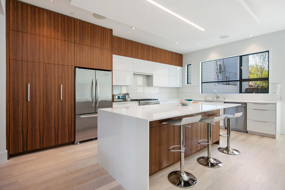 Open concept kitchen - large modern l-shaped light wood floor and beige floor open concept kitchen idea in San Francisco with a single-bowl sink, white cabinets, white backsplash, stainless steel appliances, an island, flat-panel cabinets, quartz countertops and glass sheet backsplash