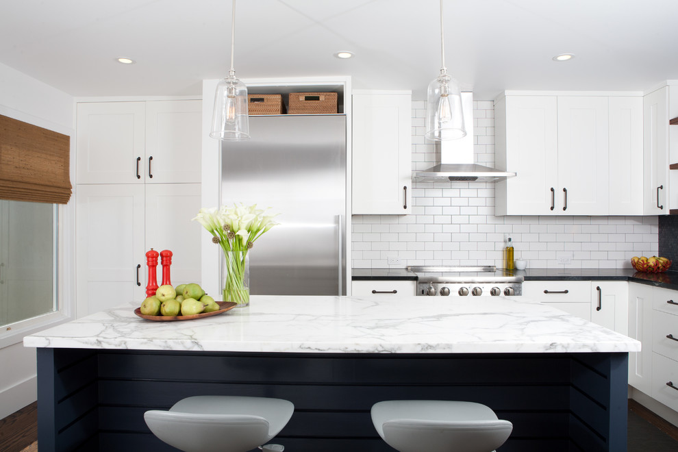 Стильный дизайн: угловая кухня-гостиная в стиле модернизм с фасадами с утопленной филенкой, белыми фасадами, фартуком из плитки кабанчик, белым фартуком и техникой из нержавеющей стали - последний тренд