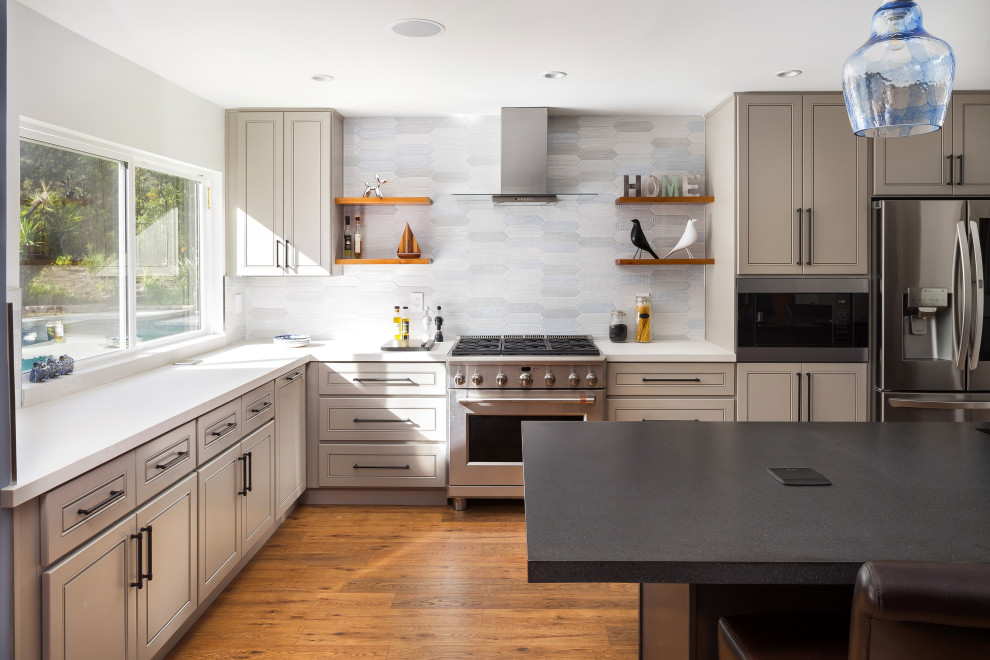Inredning av ett mellanstort grå grått kök, med en undermonterad diskho, luckor med upphöjd panel, grå skåp, bänkskiva i kvarts, flerfärgad stänkskydd, stänkskydd i porslinskakel, rostfria vitvaror, mellanmörkt trägolv, en halv köksö och brunt golv