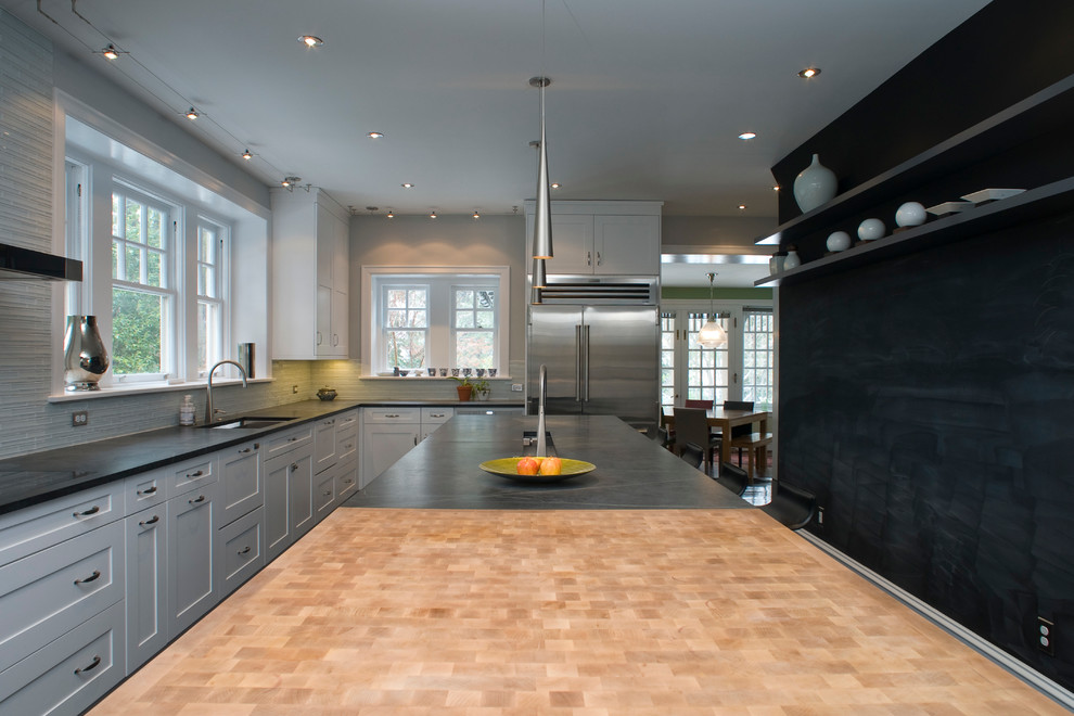 На фото: отдельная кухня в современном стиле с врезной мойкой, фасадами в стиле шейкер, деревянной столешницей, серым фартуком и техникой из нержавеющей стали