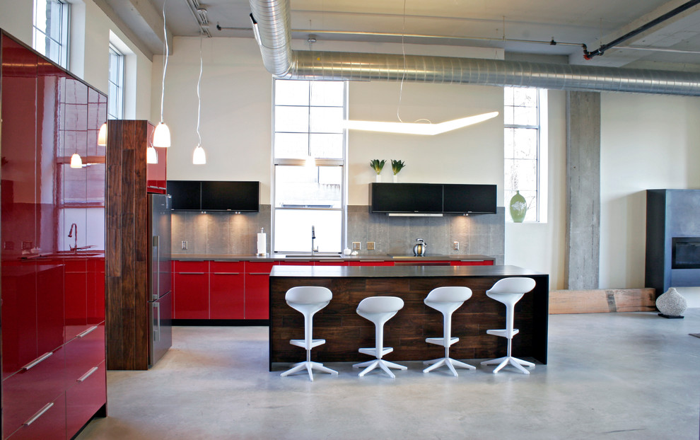 ミネアポリスにある広いインダストリアルスタイルのおしゃれなキッチン (フラットパネル扉のキャビネット、赤いキャビネット、グレーのキッチンパネル、シルバーの調理設備、コンクリートの床) の写真