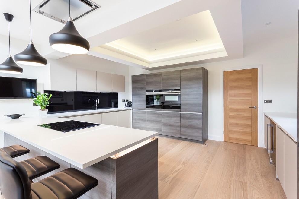 Design ideas for a medium sized contemporary u-shaped kitchen/diner in London with flat-panel cabinets, medium wood cabinets, black splashback, glass sheet splashback and a breakfast bar.