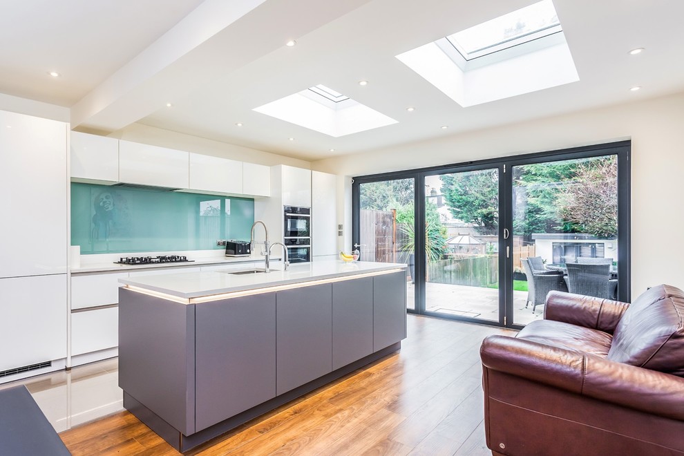 This is an example of a medium sized l-shaped open plan kitchen in London with flat-panel cabinets, grey cabinets, quartz worktops, blue splashback, glass sheet splashback and an island.