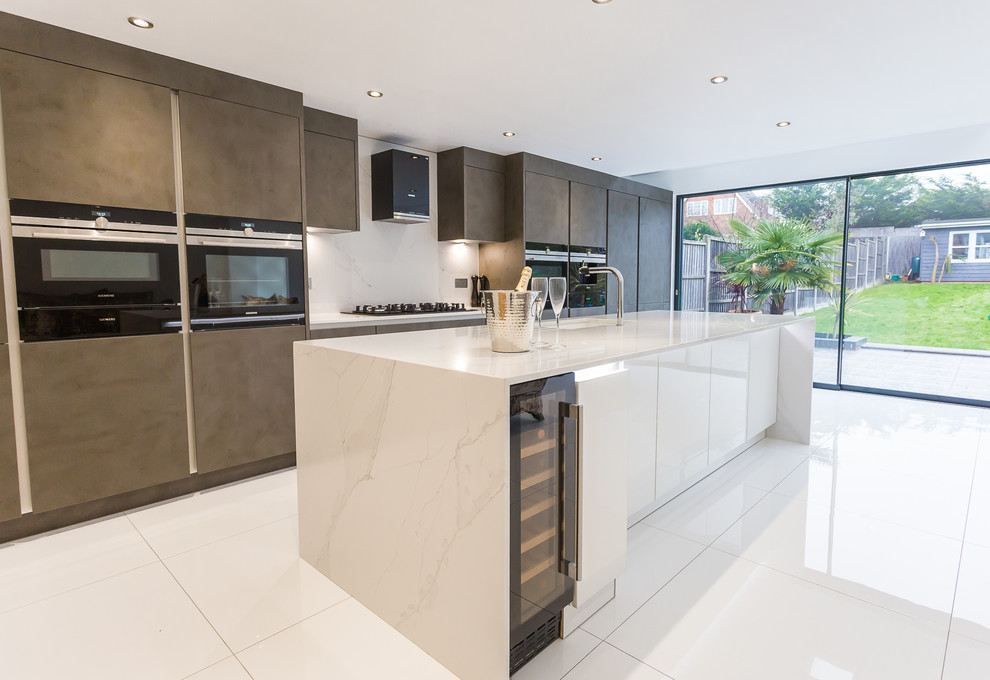 This is an example of a large modern galley open plan kitchen in London with an integrated sink, flat-panel cabinets, brown cabinets, engineered stone countertops, black appliances, an island and white worktops.