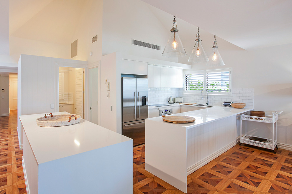 Example of a mid-sized island style u-shaped medium tone wood floor open concept kitchen design in Sunshine Coast with white cabinets, quartz countertops, yellow backsplash, subway tile backsplash, white appliances, two islands and a drop-in sink