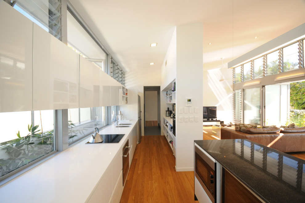 Inspiration for a coastal galley kitchen in Sunshine Coast with white cabinets, engineered stone countertops, glass sheet splashback, stainless steel appliances, medium hardwood flooring and an island.