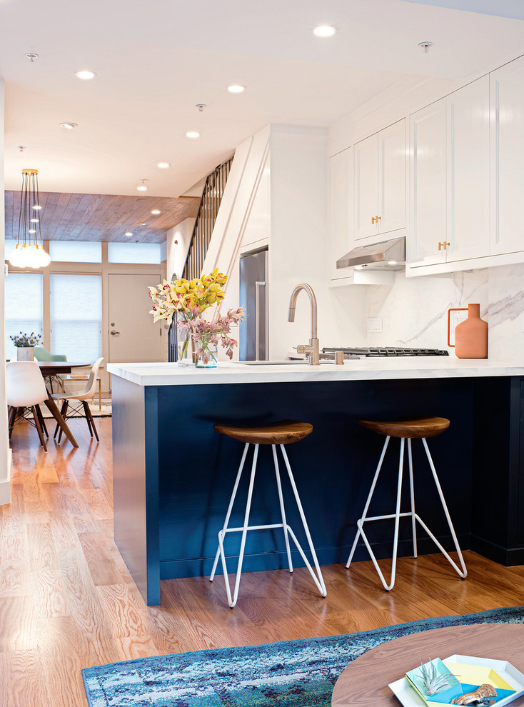 Bild på ett litet skandinaviskt kök, med en undermonterad diskho, släta luckor, blå skåp, bänkskiva i kvartsit, vitt stänkskydd, stänkskydd i sten, rostfria vitvaror och ljust trägolv