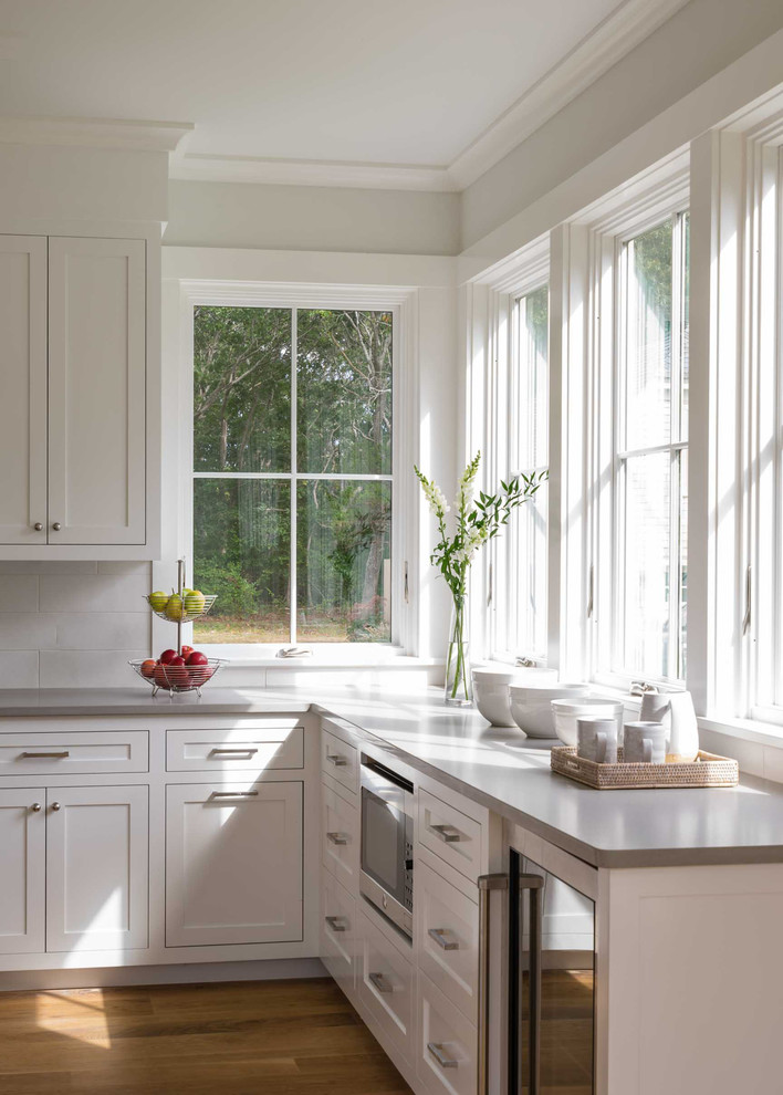 Eat-in kitchen - mid-sized transitional u-shaped light wood floor and brown floor eat-in kitchen idea in Boston with a farmhouse sink, raised-panel cabinets, white cabinets, solid surface countertops, white backsplash, subway tile backsplash, stainless steel appliances and an island