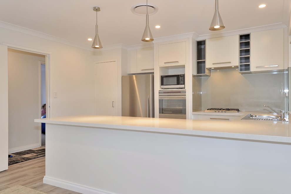 Mid-sized trendy l-shaped light wood floor and brown floor eat-in kitchen photo in Perth with a double-bowl sink, flat-panel cabinets, white cabinets, quartz countertops, gray backsplash, glass sheet backsplash, stainless steel appliances, a peninsula and white countertops