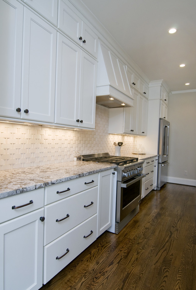 This is an example of a large classic u-shaped kitchen in Raleigh with recessed-panel cabinets, white cabinets, granite worktops, white splashback, metro tiled splashback, stainless steel appliances, medium hardwood flooring, an island and brown floors.