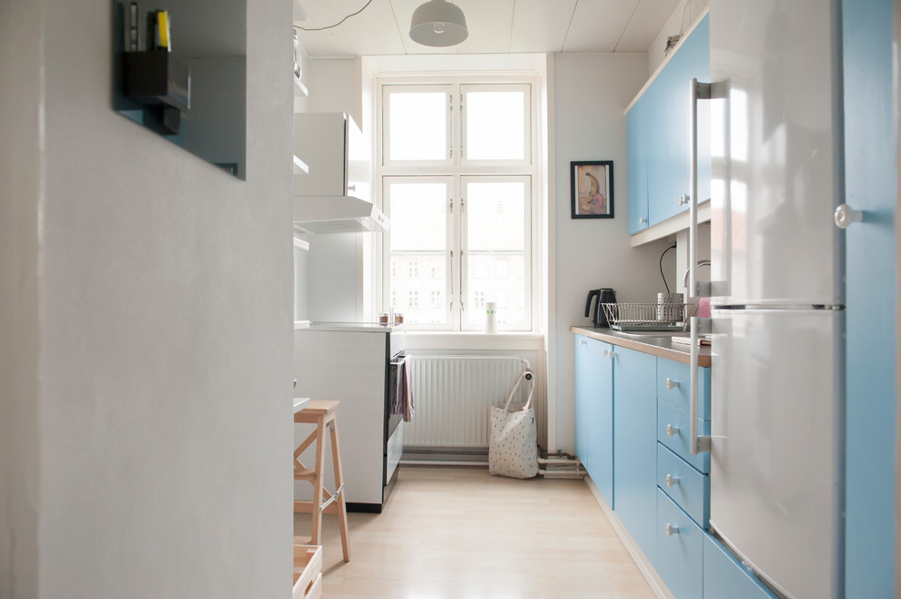 Exemple d'une cuisine parallèle scandinave fermée avec un placard à porte plane, des portes de placard bleues, un électroménager blanc, parquet clair, aucun îlot et un sol beige.