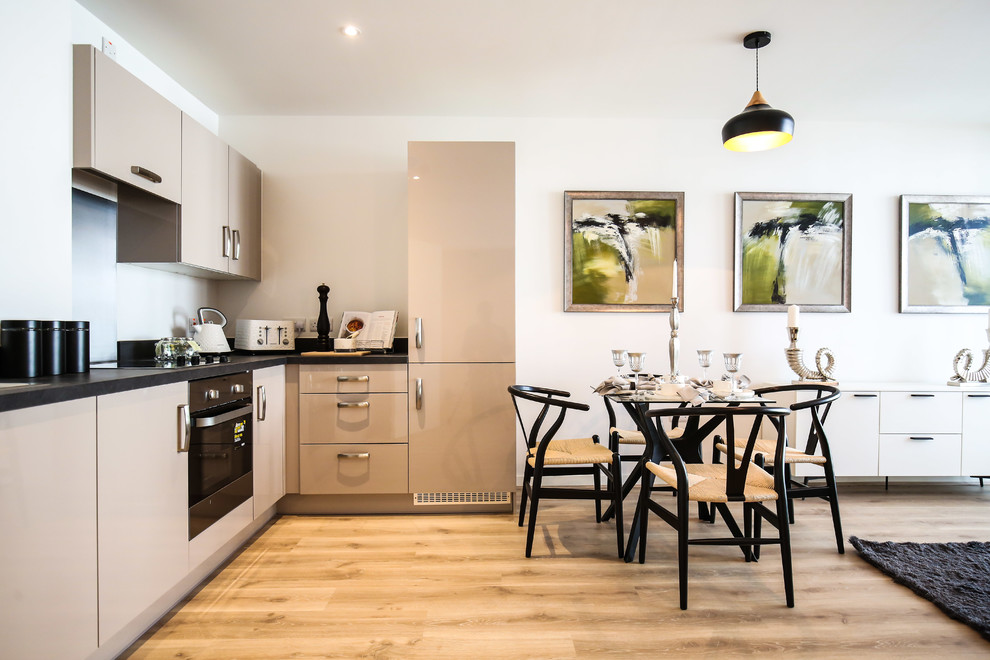 Moderne Wohnküche ohne Insel in L-Form mit flächenbündigen Schrankfronten, beigen Schränken, schwarzen Elektrogeräten und hellem Holzboden in London