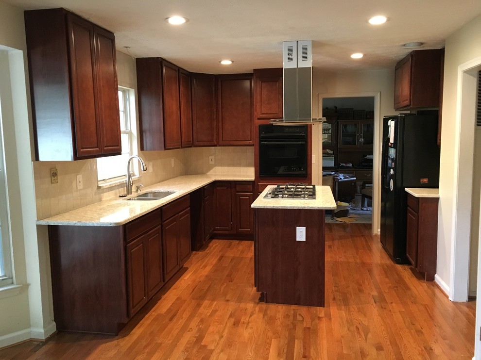 Inspiration for a large traditional u-shaped kitchen pantry in DC Metro with a submerged sink, raised-panel cabinets, brown cabinets, granite worktops, beige splashback, cement tile splashback, black appliances, light hardwood flooring and an island.