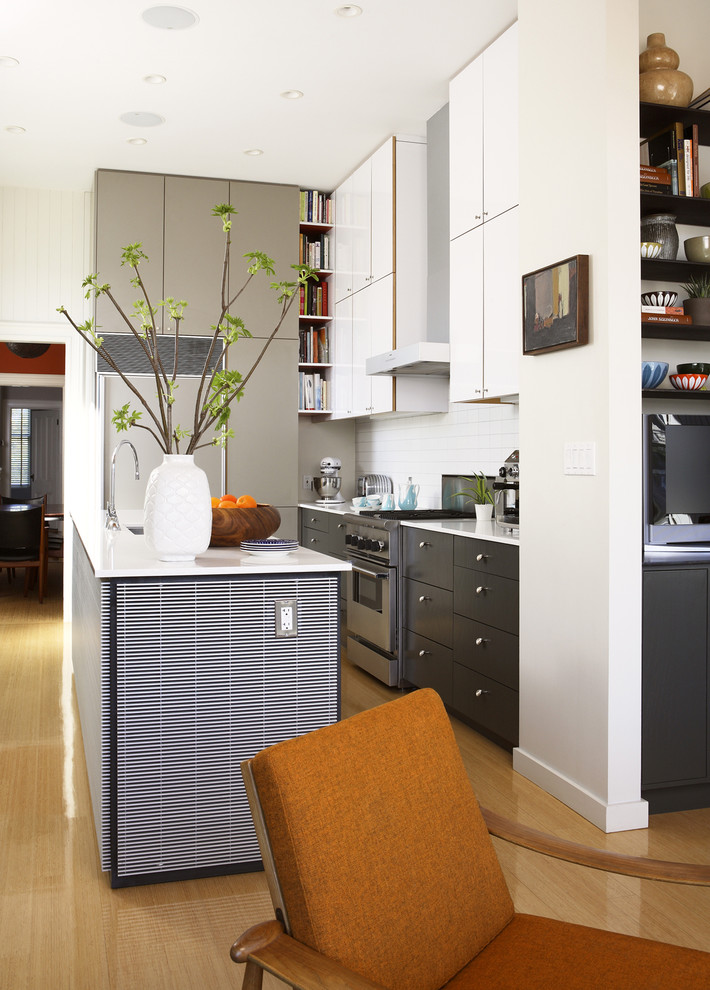 На фото: серо-белая кухня-гостиная в современном стиле с плоскими фасадами, серыми фасадами, белым фартуком и техникой под мебельный фасад с