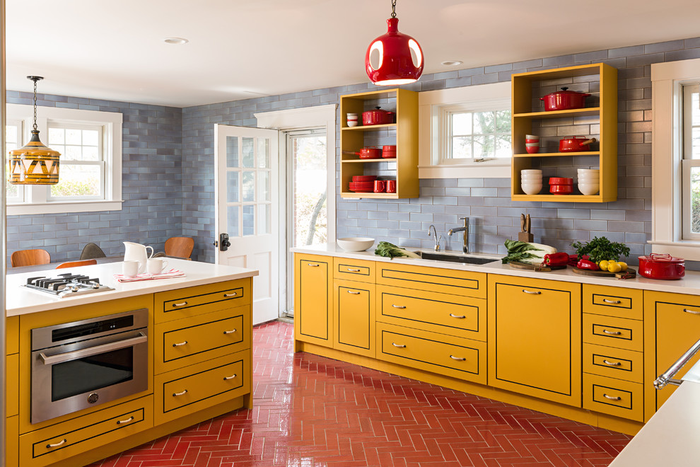 Modelo de cocina comedor contemporánea con fregadero bajoencimera, puertas de armario amarillas, salpicadero azul, electrodomésticos de acero inoxidable, una isla y armarios con paneles lisos