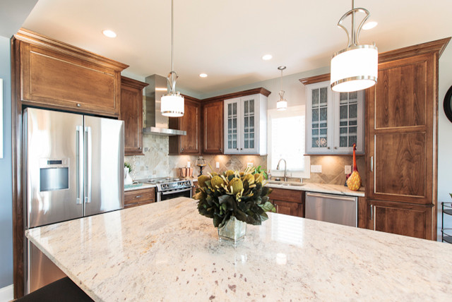 Mid-sized transitional l-shaped light wood floor open concept kitchen photo in Louisville with a double-bowl sink, recessed-panel cabinets, medium tone wood cabinets, granite countertops, beige backsplash, stone tile backsplash, stainless steel appliances and an island