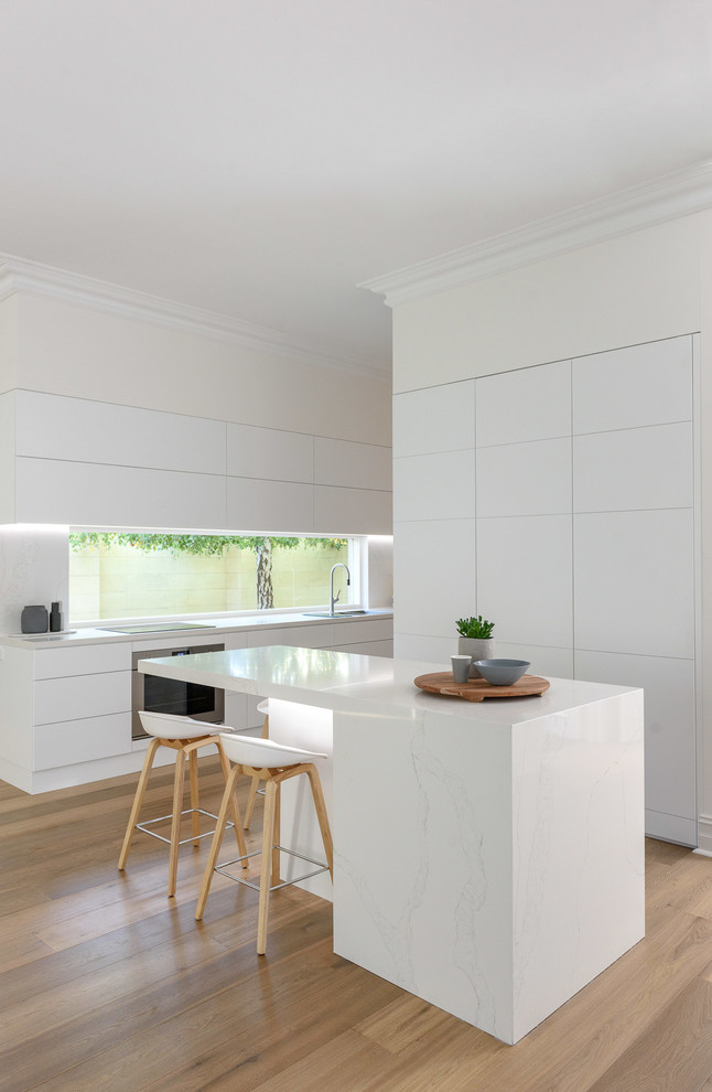 Moderne Küche mit Einbauwaschbecken, flächenbündigen Schrankfronten, türkisfarbenen Schränken, Glasrückwand, hellem Holzboden, Kücheninsel und beigem Boden in Adelaide