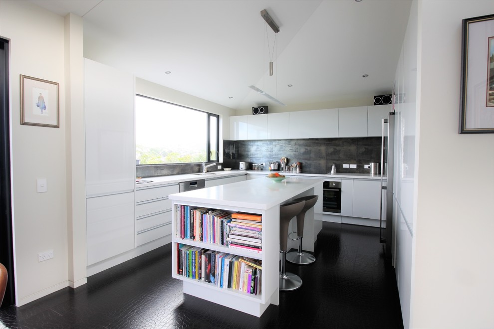 Enclosed kitchen - contemporary l-shaped black floor enclosed kitchen idea in Wellington with flat-panel cabinets, white cabinets, gray backsplash, paneled appliances and an island