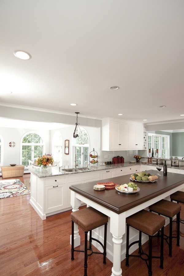 Inredning av ett klassiskt stort kök, med en undermonterad diskho, luckor med infälld panel, vita skåp, bänkskiva i kvartsit, grönt stänkskydd, stänkskydd i glaskakel, rostfria vitvaror, mellanmörkt trägolv och en köksö