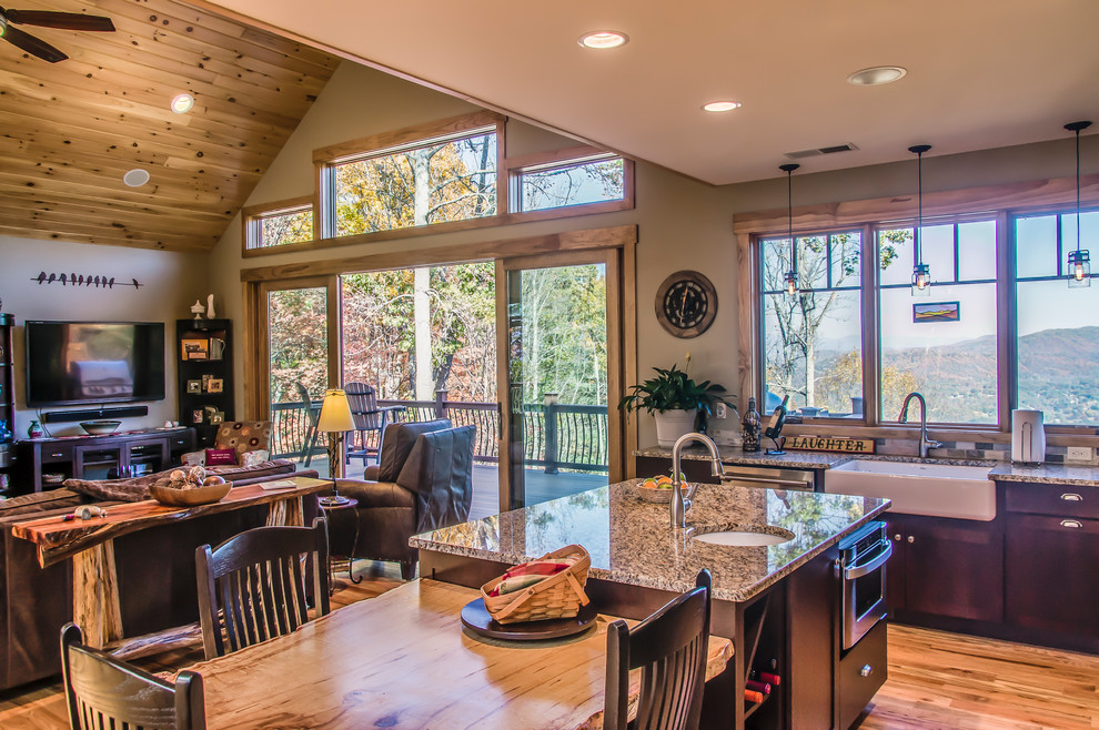 Large rustic l-shaped open plan kitchen in Other with a belfast sink, shaker cabinets, dark wood cabinets, granite worktops, beige splashback, stone tiled splashback, stainless steel appliances, an island, beige worktops, medium hardwood flooring and brown floors.