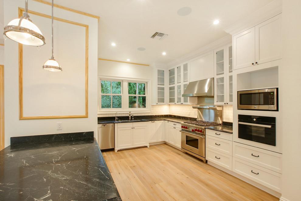 Photo of a medium sized nautical u-shaped kitchen/diner in Miami with a belfast sink, white cabinets, wood worktops, white splashback, metro tiled splashback, stainless steel appliances, light hardwood flooring and a breakfast bar.