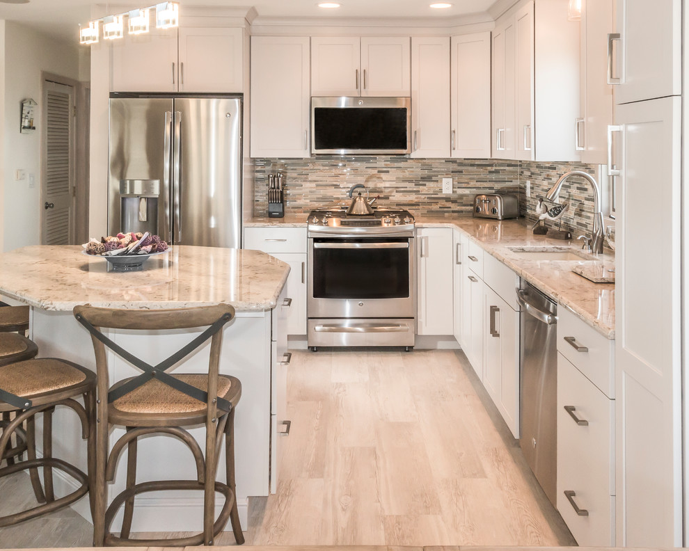 Open concept kitchen - large transitional l-shaped ceramic tile and beige floor open concept kitchen idea in New York with a drop-in sink, recessed-panel cabinets, white cabinets, granite countertops, metallic backsplash, stone tile backsplash, stainless steel appliances and an island