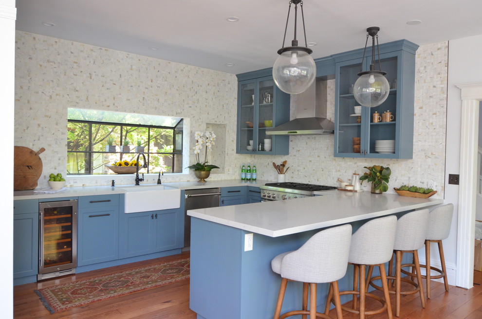 Inredning av ett klassiskt mellanstort grå grått kök, med en rustik diskho, luckor med glaspanel, blå skåp, rostfria vitvaror, mellanmörkt trägolv, en halv köksö, bänkskiva i kvarts, brunt golv, vitt stänkskydd och stänkskydd i marmor