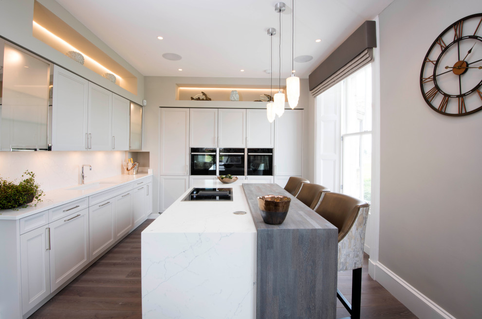 This is an example of a large classic l-shaped kitchen in Other with a submerged sink, shaker cabinets, white cabinets, white splashback, black appliances, medium hardwood flooring, an island, brown floors and white worktops.