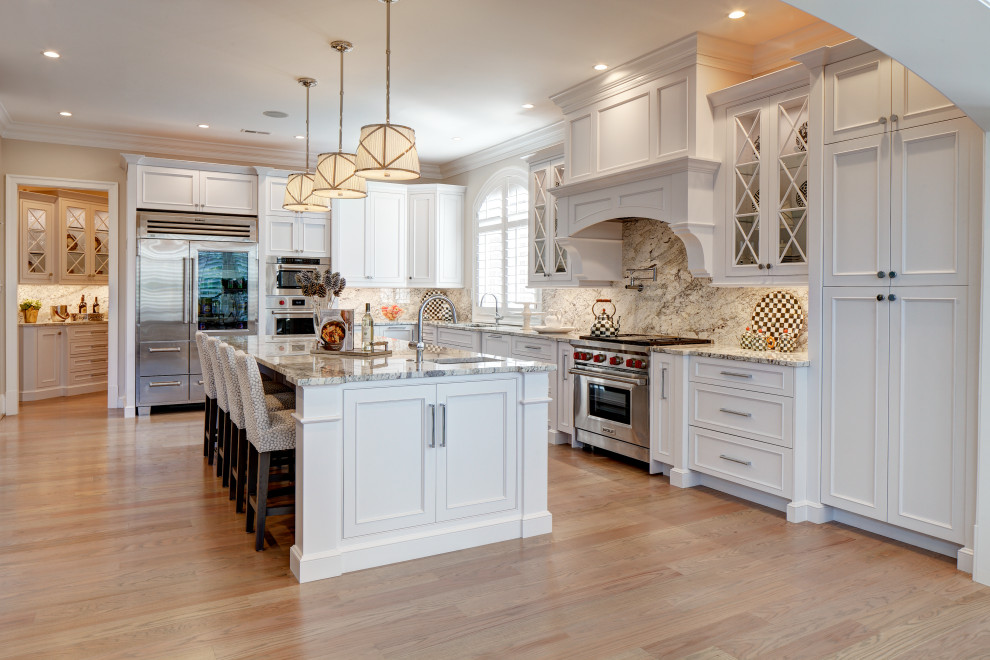 Large traditional l-shaped kitchen pantry in DC Metro with a submerged sink, recessed-panel cabinets, white cabinets, granite worktops, stainless steel appliances, medium hardwood flooring, an island and beige floors.