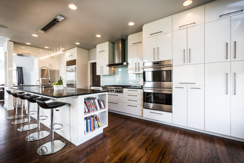 Medium sized contemporary kitchen in Boise with flat-panel cabinets, white cabinets, glass sheet splashback, stainless steel appliances, an island, blue splashback and dark hardwood flooring.