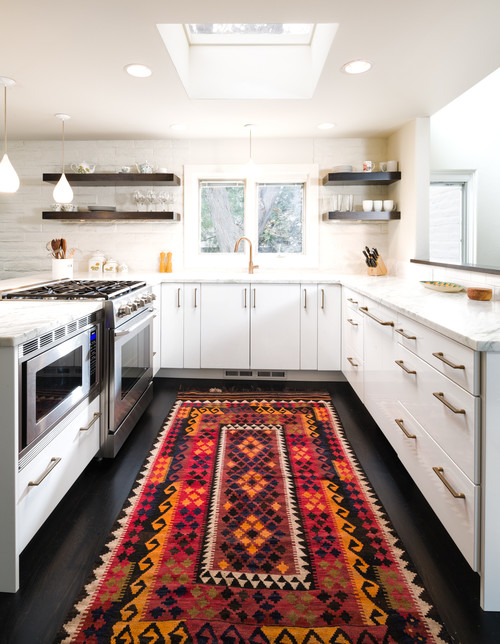 Modern Canadian kitchen with sleek white cabinets, brass handles, open shelving, marble countertops, and a vibrant patterned rug, showcasing one of the best kitchen cabinet color trends in Canada.