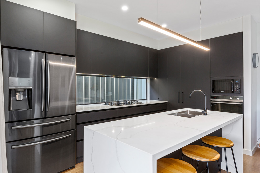 Moderne Küche mit Doppelwaschbecken, flächenbündigen Schrankfronten, schwarzen Schränken, Rückwand-Fenster, Küchengeräten aus Edelstahl, hellem Holzboden, Kücheninsel und weißer Arbeitsplatte in Adelaide