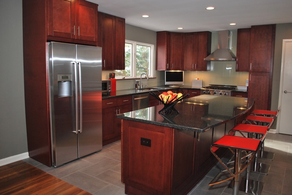 Mid-sized trendy l-shaped cement tile floor and gray floor enclosed kitchen photo in New York with an undermount sink, shaker cabinets, red cabinets, granite countertops, beige backsplash, glass tile backsplash, stainless steel appliances, an island and black countertops